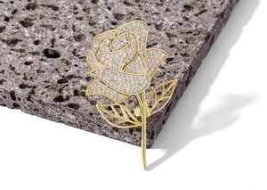 Macro detail of elegant gold rose brooch with sparkling zircon petals on dark slate