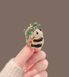 Detail of a panda brooch with crystals, black enamel and green bamboo leaves held by hand