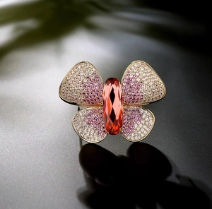 Detailed macro view of a luxury gold butterfly brooch with orange gemstone and pavé stones