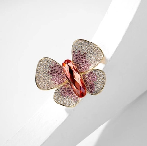 Macro detail of butterfly brooch with orange crystal and purple gradient pave setting