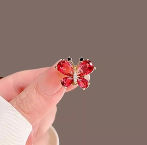 Detailed close-up of a crystal butterfly brooch featuring pear-cut red gems and gold plating