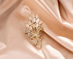 Détail d'une broche fleur dorée avec pierres d'opale et cristaux sur du tissu de soie