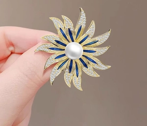 Detailed macro view of sunflower brooch with white pearl, blue enamel, and gold plating
