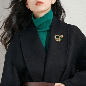 Broche géométrique vintage avec pierres vertes et perle sur pull vert foncé