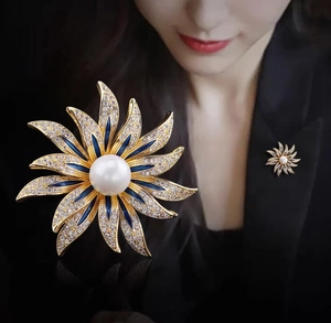 Detailed view of sunflower brooch with blue enamel petals and a center pearl on blazer