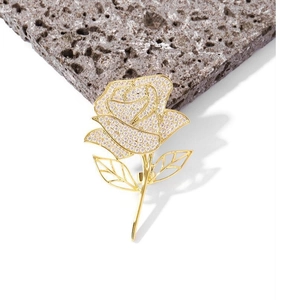 Elegant rose brooch with white zircons and golden petals on grey textured stone