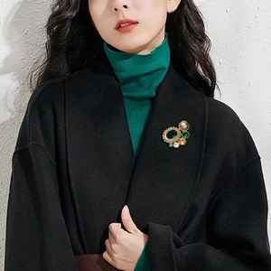 Broche géométrique vintage avec pierre verte et perles sur un élégant manteau noir