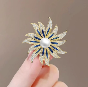 Macro view of sunflower brooch with blue enamel petals, white pearl, and gold plating