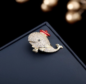 Macro shot of whale brooch with cubic zirconia crystals and small red enamel hat