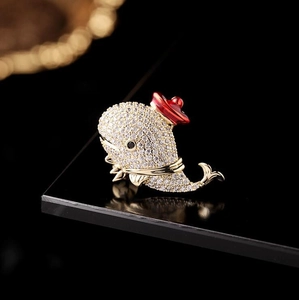Macro shot of gold-plated whale brooch with pavé zircon crystals and red enamel hat detail