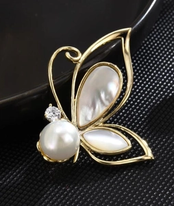 Macro detail of butterfly brooch showing iridescent shell wings and white pearl center