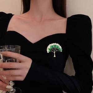 Élégante broche sapin de Noël dorée avec cristaux verts et blancs sur une robe noire