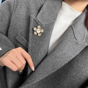 Broche fleur dorée élégante avec perle centrale sur le revers d'un manteau gris