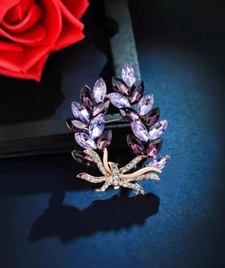 Detail of wreath-shaped brooch with purple marquise crystals and pavé bow on dark blue background