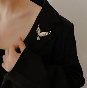 Detail einer goldenen Flügelbrosche mit Zirkonen und lilafarbenem Edelstein auf einem Blazer