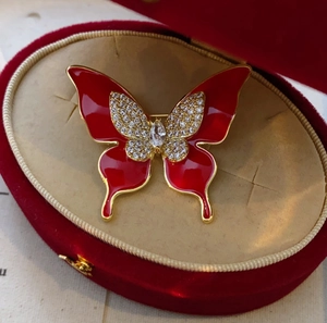 Détail d'une broche papillon rouge avec émail et zircons dans une boîte en velours