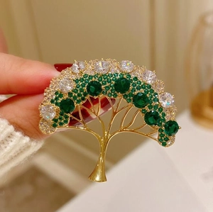 Broche arbre dorée avec cristaux verts étincelants et zircons tenue à la main