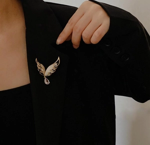 Detailaufnahme der goldenen Flügelbrosche mit Kristallen und fliederfarbenem Tropfen