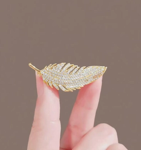 Dettaglio spilla dorata a forma di piuma con cristalli per abiti e accessori eleganti