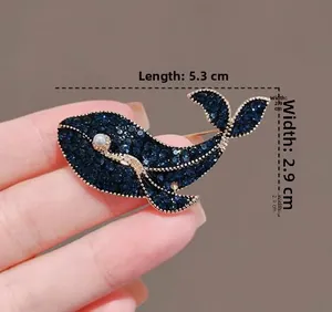 Détail d'une broche baleine en cristal bleu foncé avec bordure dorée et oeil perlé