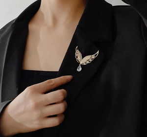 Detail einer goldenen Flügelbrosche mit Strasssteinen und Kristalltropfen auf einem Blazer