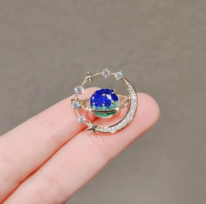 Detailed close-up of celestial brooch with blue enamel planet and crescent moon star design