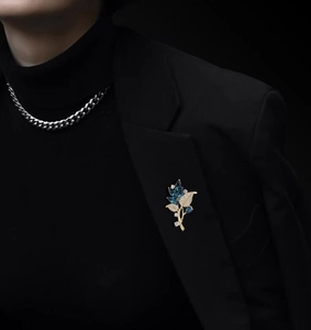 Detailed view of an elegant gold orchid leaf brooch with blue gems on a black suit lapel