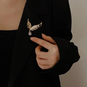 Detail einer goldenen Flügel-Brosche mit Kristall-Wassertropfen auf schwarzem Blazer