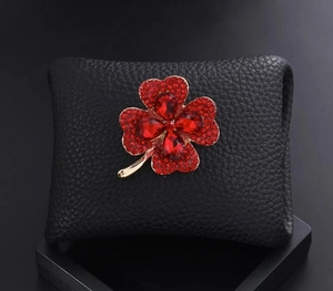 Détail de la broche trèfle rouge sertie de rubis étincelants sur cuir texturé noir