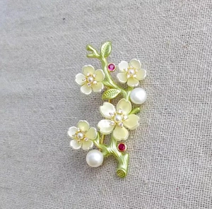 Detail of peach blossom branch brooch with white pearls and red gems on linen fabric