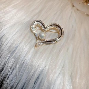 Close-up of heart-shaped gold brooch with inlaid zircon and a large center pearl