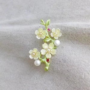 Elegant peach blossom branch brooch with green enamel, white petals, and pearls on linen