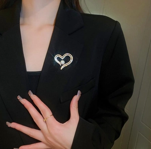 Detailed view of a gold heart brooch with zircons and pearl on a black suit lapel