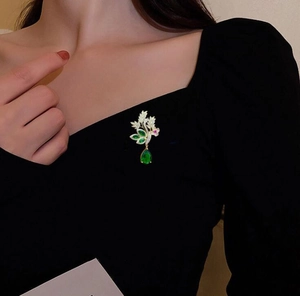 Gros plan sur la broche feuille dorée avec gemmes vertes sur un tissu noir chic