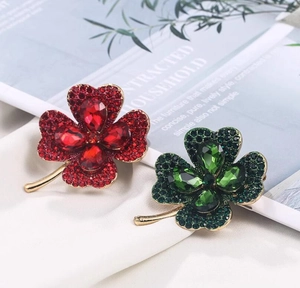 Détail de broches trèfle rouges et vertes avec cristaux scintillants sur métal doré