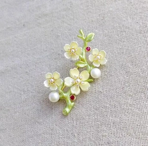 Elegant peach blossom branch brooch with white petals, pearls, and crystals on linen
