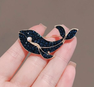 Détails d'une broche baleine bleue avec cristaux scintillants et perle blanche fine