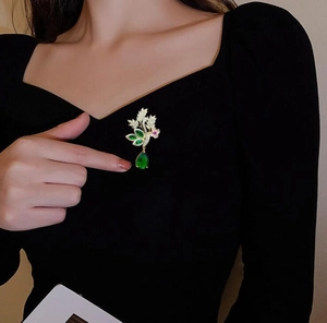 Détail de la broche fleurie avec goutte d'émeraude verte sur un vêtement noir