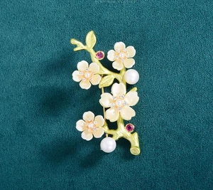 Macro shot of peach blossom brooch with white enamel flowers and red crystal accents