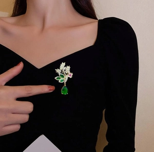 Gros plan d'une broche fleur vintage avec gemmes vertes et cristaux sur robe noire