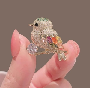 Macro detail of bird brooch with colorful marquise crystals on a golden branch