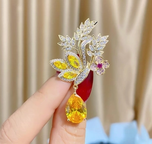 Détail d'une broche florale dorée avec cristaux jaunes et accents de fleurs roses