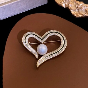 Macro shot of heart pearl brooch with gold frame, white zircons, and black enamel detail