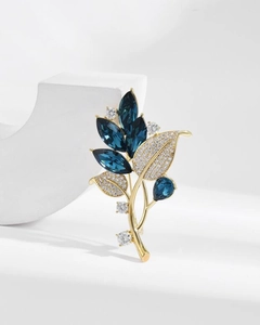 Detailed close-up of an elegant gold leaf brooch with navy blue crystals and zircons
