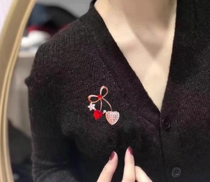 Dettaglio di un'elegante spilla a cuore ciliegia con cristalli su un cardigan nero