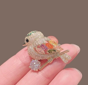 Close-up of a colorful bird brooch with sparkling gems and crystals held in hand