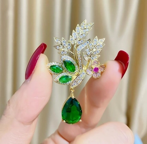 Détail d'une broche fleurie dorée avec une grande gemme verte en goutte et des zircons