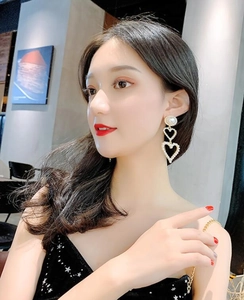 Detail of heart-shaped pearl drop earrings with rhinestones on a female model