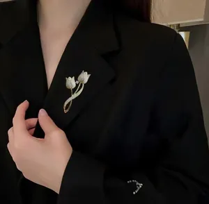 Détail d'une broche tulipe dorée avec cristaux sur le revers d'un blazer noir