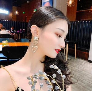 Close-up of long bridal earrings with pearls and heart tassels worn by a model